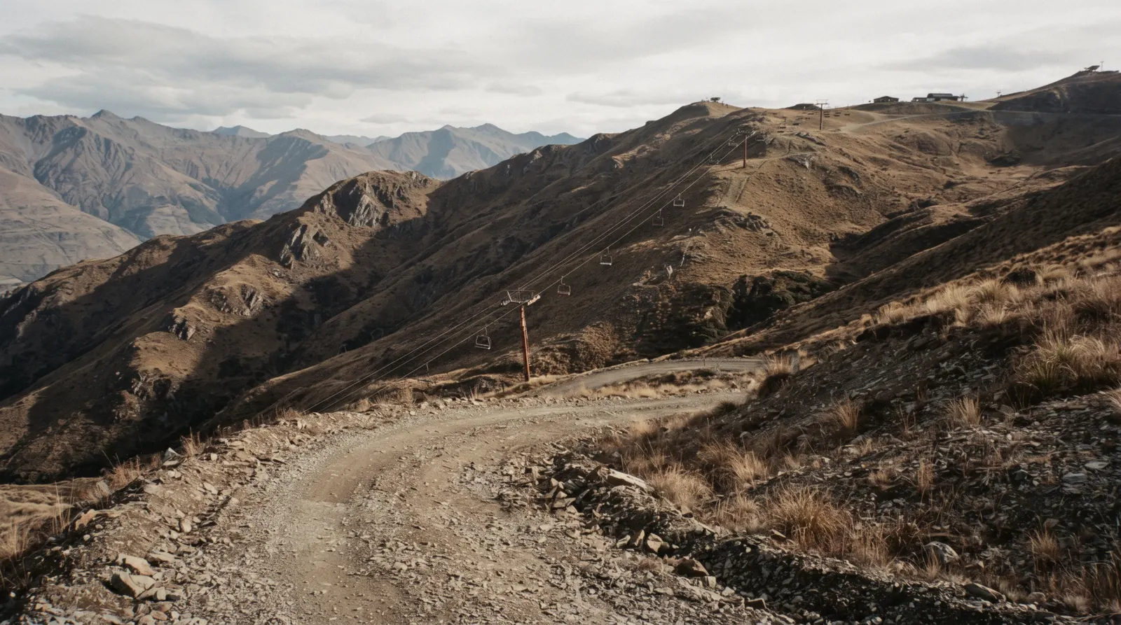 The brown tussock ridges and chairlift line of Coronet Peak above the access road in late afternoon light, Queenstown, New Zealand