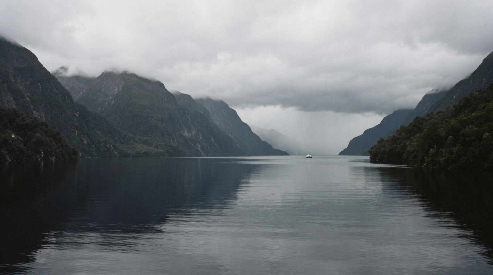 A wilderness cruise boat under cloud on a still arm of the fiord on a Doubtful Sound day trip from Queenstown, New Zealand