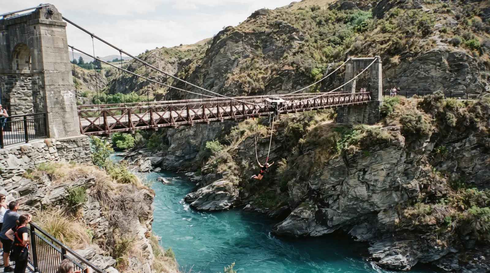 The 1880 suspension bridge over the green Kawarau River with a jumper falling from the platform at the Kawarau Bridge bungy, Queenstown, New Zealand