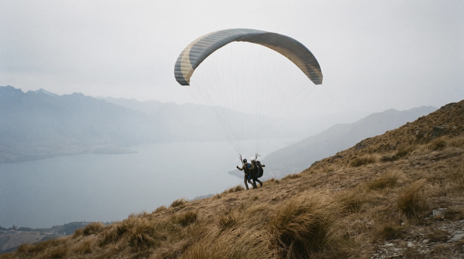 A tandem paraglider turning above the Wakatipu Basin with snow on the peaks behind, paragliding in Queenstown, New Zealand