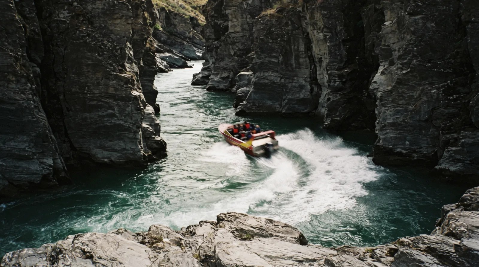 A red Shotover Jet boat spinning against the canyon walls of the Shotover River near Queenstown, New Zealand