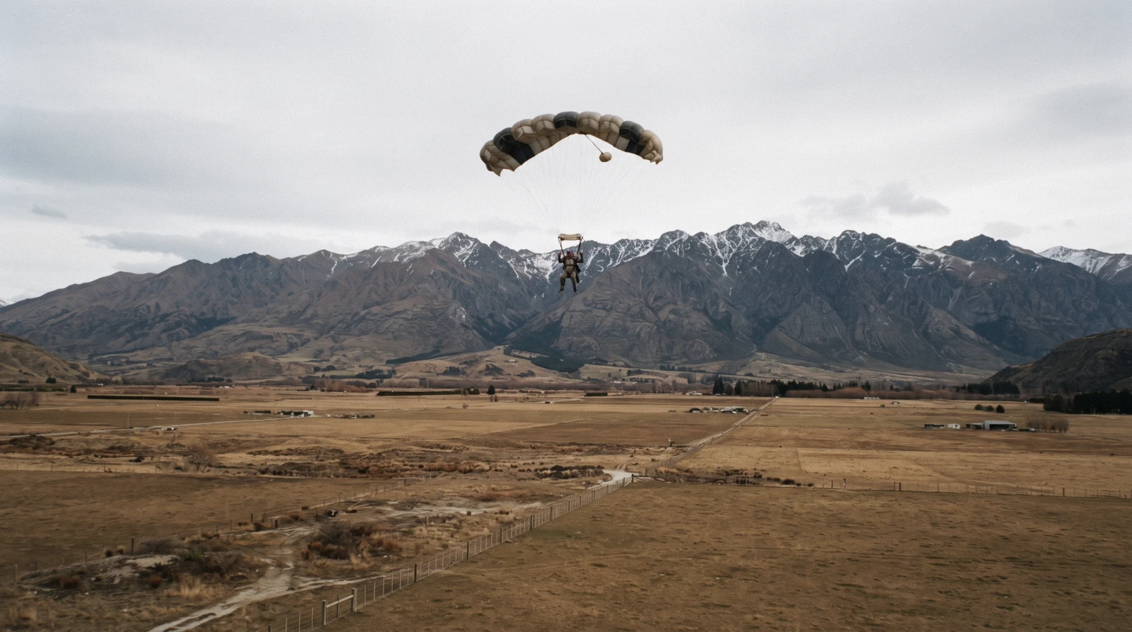 A tandem pair in freefall over the Wakatipu Basin with The Remarkables behind them, skydiving in Queenstown, New Zealand