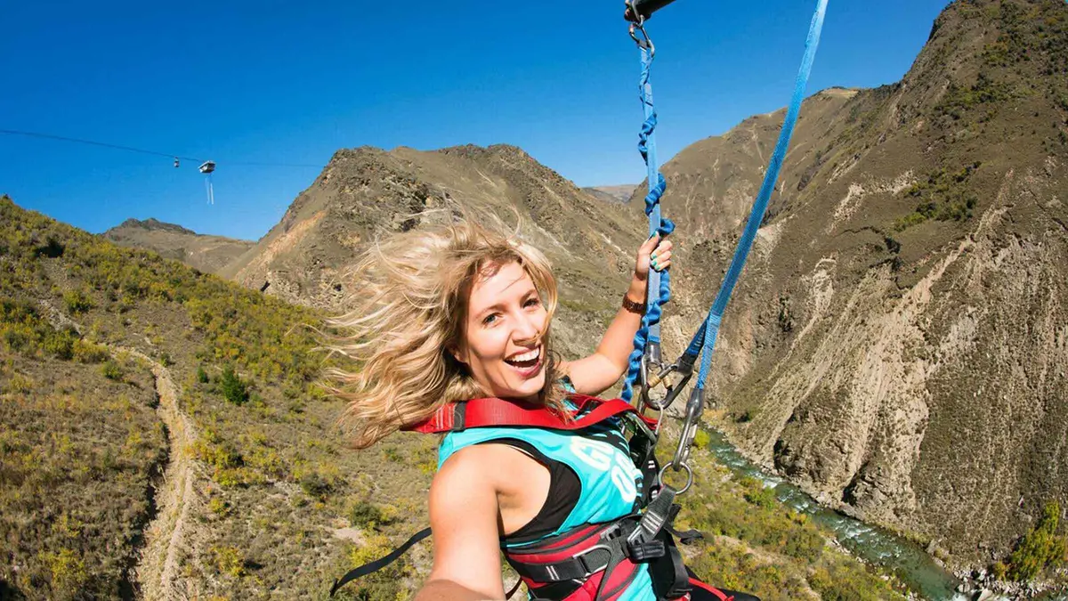 A tandem pair arcing across the Nevis valley on the swing — Nevis Bungy, Queenstown, New Zealand