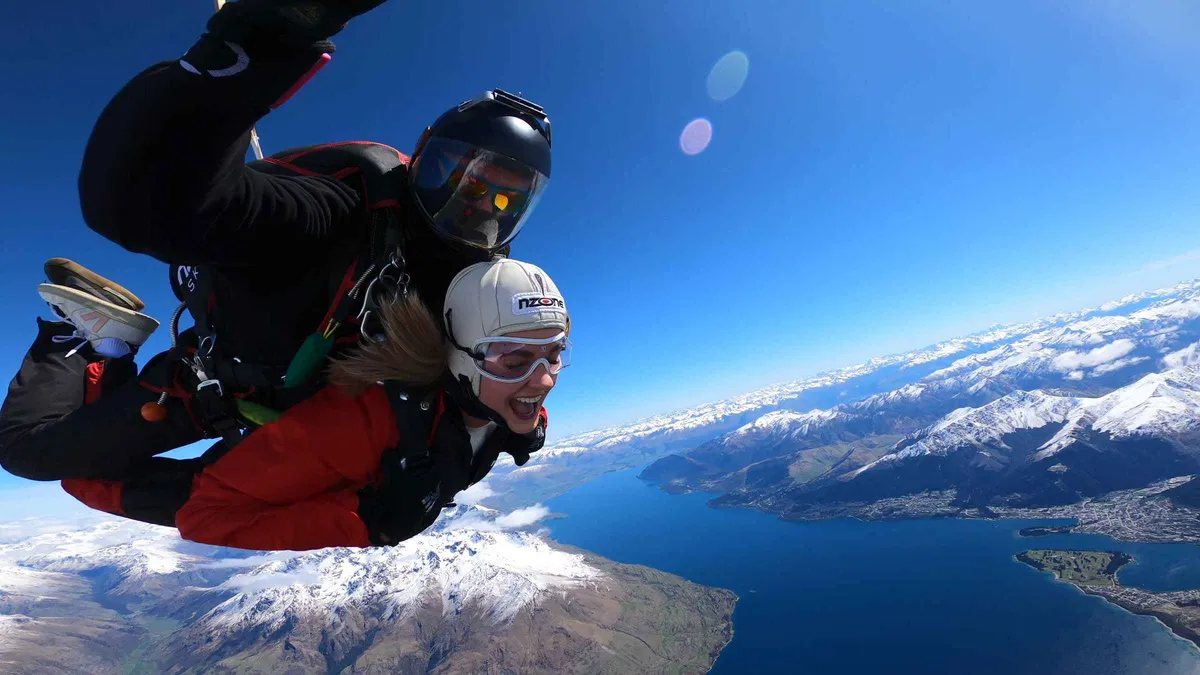 A tandem pair in freefall above snow-capped Southern Lakes peaks — skydiving in Queenstown, New Zealand