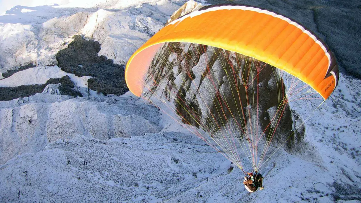 A paraglider launching from snow at the top of Coronet Peak — paragliding in Queenstown, New Zealand