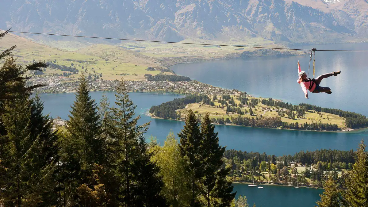 A rider on a treetop zipline platform above Lake Wakatipu — Ziptrek Queenstown ziplining, New Zealand