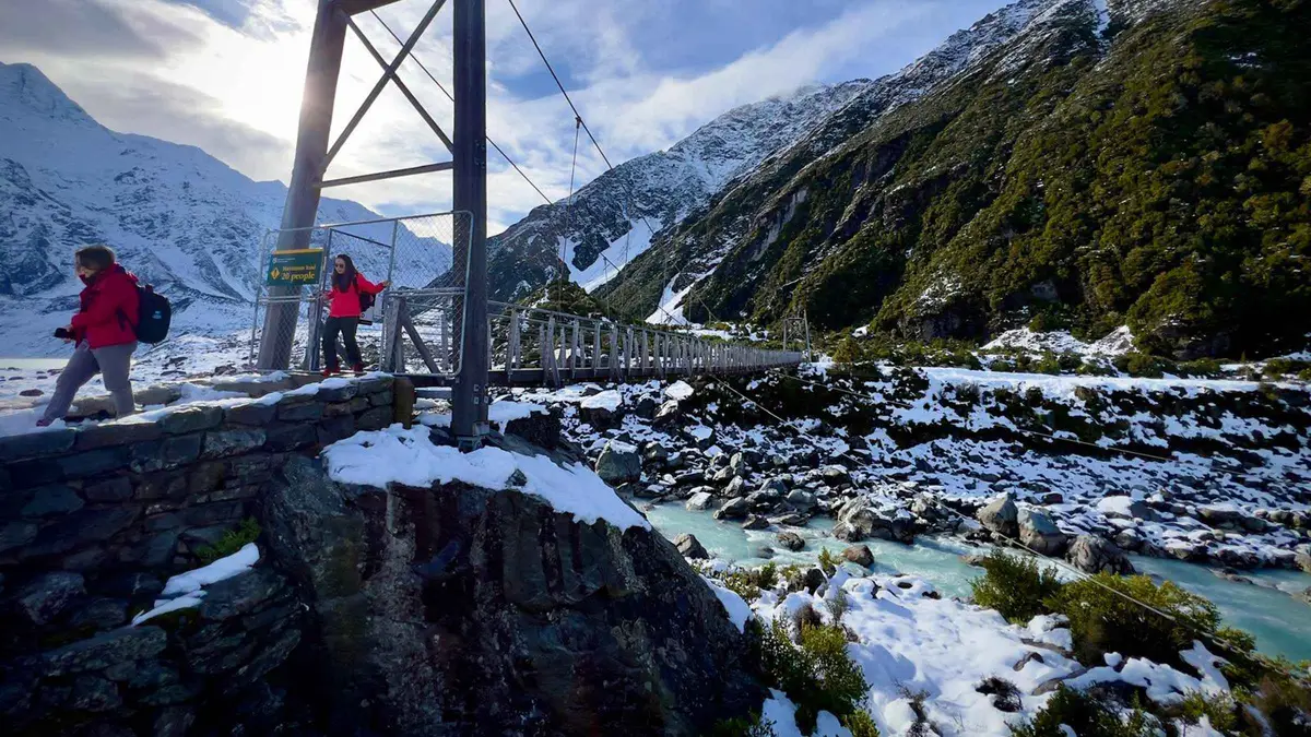 Walkers on the Hooker Valley swing bridge below Aoraki — Mount Cook from Queenstown, New Zealand